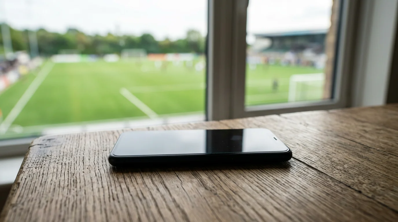 Smartphone sobre una mesa junto a un campo de fútbol con césped verde de fondo
