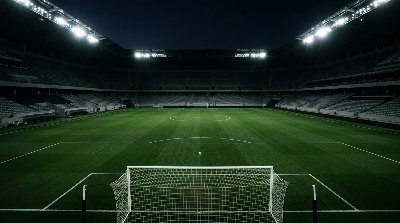 Estadio de fútbol vacío con un balón de fútbol en el centro del campo iluminado por focos nocturnos